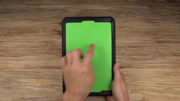 Une femme tient une tablette PC avec un écran vert pour votre propre contenu personnalisé sur fond de table en bois 