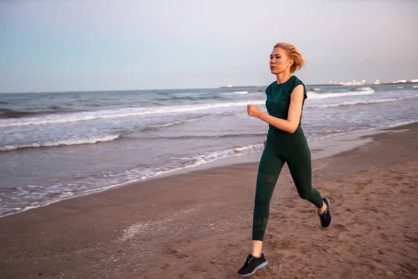 Beautiful people Fitness woman with short blonde hair running in a sea beach side . Sport and Healthy Lifestyle Concept