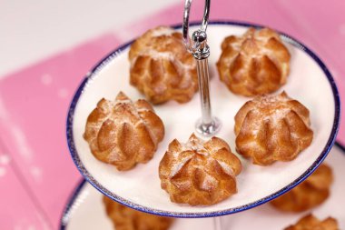 Pembe bir arka plan üzerinde güzel bir platform üzerinde pudra şekeri ile taze pişmiş eclairs.