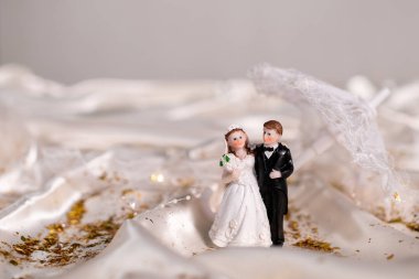 bej saten kumaş üzerinde yeni evlilerin seramik figürleri, arka planda dantel bir şemsiye