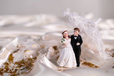 bej saten kumaş üzerinde yeni evlilerin seramik figürleri, arka planda dantel bir şemsiye