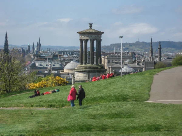 爱丁堡 苏格兰 2014 Dugald 斯图尔特纪念碑的看法与草和人坐它 城市典型的大厦在背景上 在爱丁堡 — 图库照片