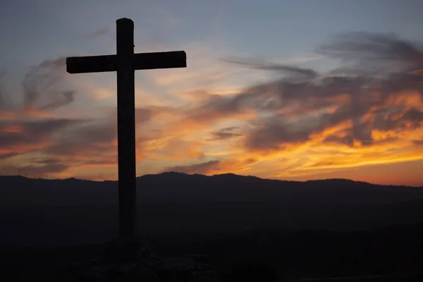 Religion theme, view of catholic cross in black shadow, with fantastic sunset with warm colors and mountains as background, in Viseu, Portugal