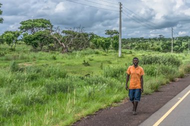 Malange / Angola - 12 08 2018: bitki örtüsü ve arka plan olarak bulutlu gökyüzü ile yol boyunca yürüyen bir adam görünümü