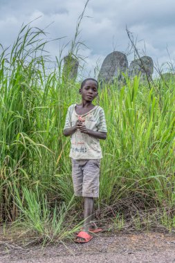 Malange / Angola - 12 08 2018: View of poor african boy, very expressive, tropical landscape as background, in Angola clipart