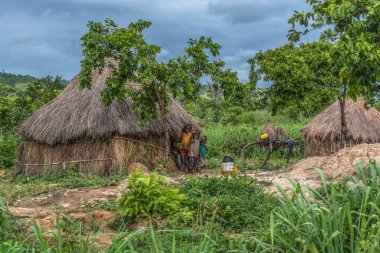 Malange / Angola - 12 08 2018: geleneksel köy, çocuklar üzerinde tebrik görünümünü thatched çatı ile ev ve pişmiş toprak ve saman duvarlar, bulutlu gökyüzü arka plan olarak