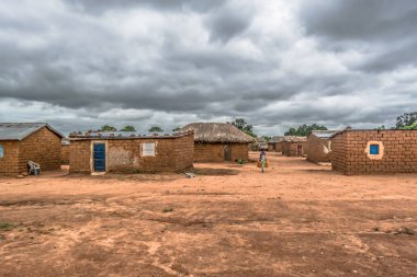 Malange / Angola - 12 08 2018: geleneksel köy, yolda, su kapları taşıyan kadın görünümünü thatched evlerin çatı ve pişmiş toprak ve saman duvarlar, bulutlu gökyüzü arka plan olarak