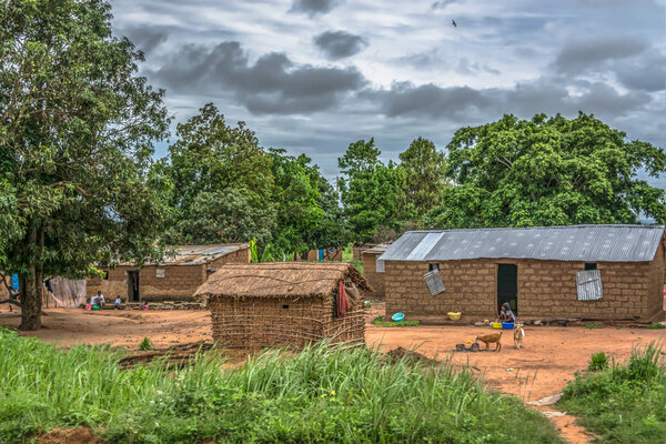 Malange / Angola - 12 08 2018: View of traditional village, people and thatched and zinc sheet on roof houses and terracotta brick walls, cloudy sky as background, in Angola