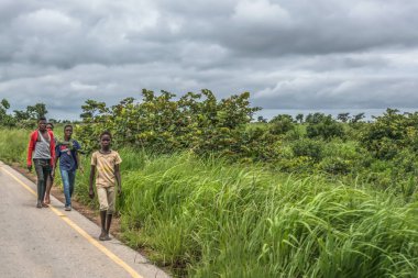 Malange / Angola - 12 08 2018: bir grup genç erkek arka plan olarak yol kenarı, tropikal peyzaj boyunca yürüyüş, görünümünü