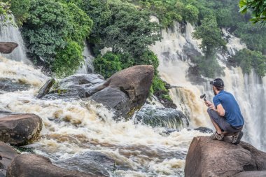 Malange / Angola - 12 08 2018: Kalandula çağlayanbir kaya üzerinde, bir aksiyon kamerası ile filme, dizlerinin üzerinde adam görünümü