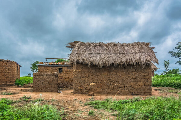 View of traditional village, house thatched on roof and terracotta walls, dramatic cloudy sky as background, in Angola