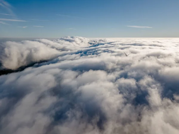 View of a drone above the fog, wind turbines with fog and blue sky