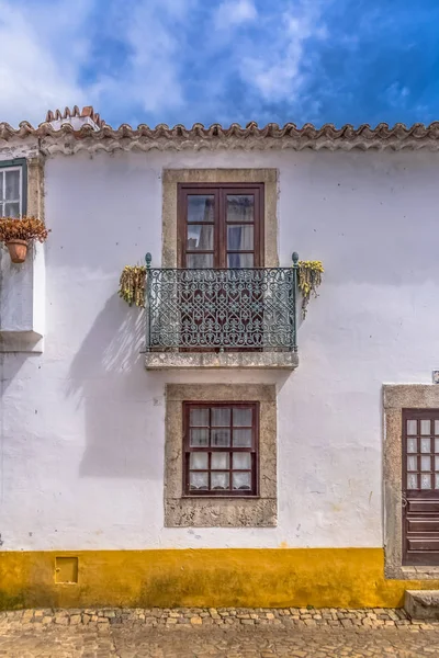 View of a Portuguese vernacular facade with balcony and flowers around windows, on medieval village of ��bidos — стокове фото