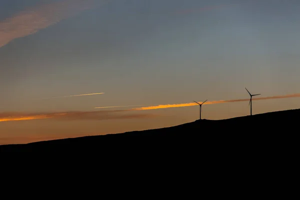 Silhouette view of a wind turbines on top of mountains, sunset sky