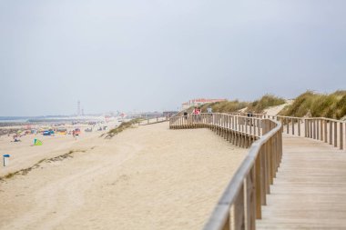 Sahilde yaya ahşap yol görünümü, insanlar yürüyüş ve insanlar sahilde güneşlenme alarak, arka plan olarak deniz feneri