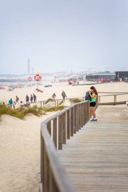 Sahilde yaya ahşap yol görünümü, insanlar yürüyüş ve insanlar sahilde güneşlenme alarak, arka plan olarak deniz feneri
