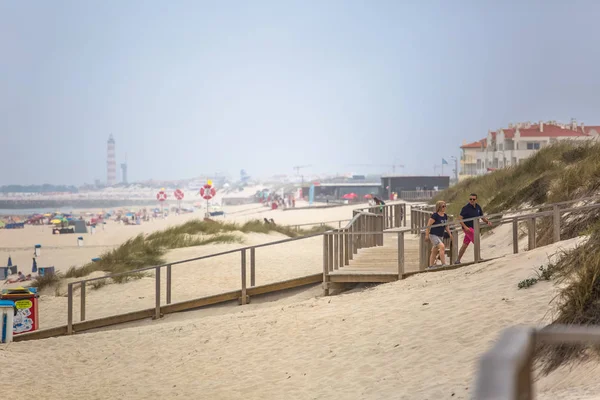 Sahilde yaya ahşap yol görünümü, insanlar yürüyüş ve insanlar sahilde güneşlenme alarak, arka plan olarak deniz feneri