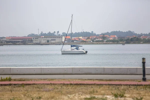 Uitzicht op de rivier de Aveiro met privé-recreatieve boot met mensen zeilen. Dag met wolken en achtergrond met typische vegetatie en gebouwen — Stockfoto