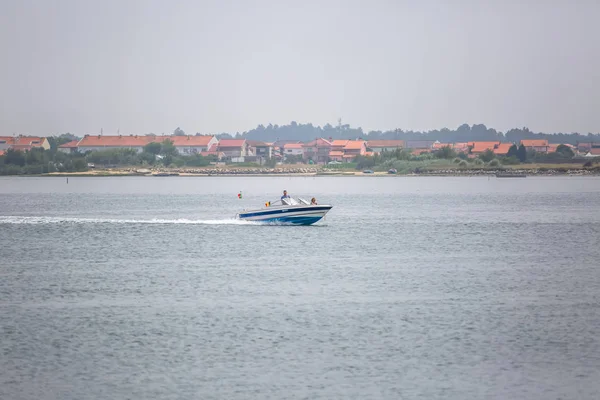 Uitzicht op de rivier de Aveiro met privé-recreatieve boot met mensen zeilen. Dag met wolken en achtergrond met typische vegetatie en gebouwen — Stockfoto