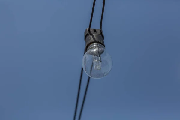 Vista de uma antiga lâmpada incandescente, com fio exterior na rua com fundo azul céu — Fotografia de Stock