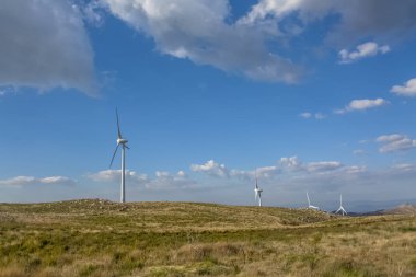 Dağların tepesindeki rüzgar türbinlerinin görüntüsü, arkaplan olarak mavi gökyüzü