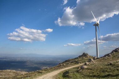 Dağların tepesinde bir rüzgar türbini, arka planda mavi gökyüzü