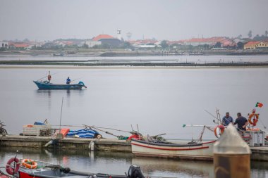 İnsanlar yelken ile balıkçı tekne ile Aveiro nehri görünümü. Tipik bitki örtüsü ve binalar ile bulutlar ve arka plan ile Gün