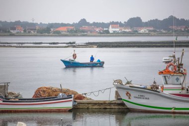 İnsanlar yelken ile balıkçı tekne ile Aveiro nehri görünümü. Tipik bitki örtüsü ve binalar ile bulutlar ve arka plan ile Gün