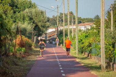 Viseu / Portugal - 10 05 2018: Çevresel yaya / bisiklet şeridi manzarası, insanlar köpekle koşuyor ve yürüyor, ağaçlar köyü arka plan olarak