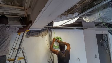 İki Afrikalı inşaat işçisi, bir inşaat sahasına elektrik kabloları döşeyen elektrikçiler görülüyor....