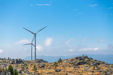 Dağların tepesindeki rüzgar türbinlerinin görüntüsü, arkaplan olarak bulutlu gökyüzü...