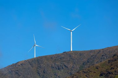 Dağların tepesindeki rüzgar türbinlerinin görüntüsü, arkaplan olarak bulutlu gökyüzü...