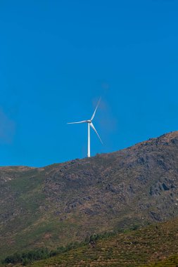 Dağların tepesinde bir rüzgar türbini, Portekiz 'de arka plan olarak mavi gökyüzü
