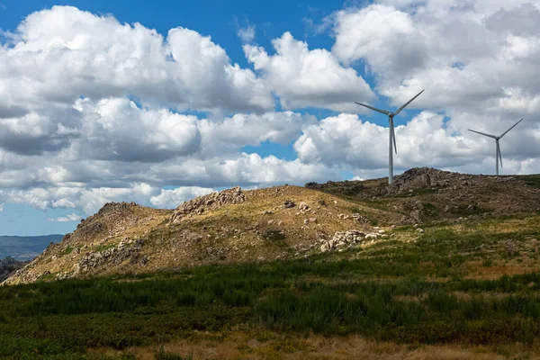 Dağların tepesindeki rüzgar türbinlerinin manzarası, toprak yol ve vahşi doğa ve manzara, arka plan olarak bulutlu gökyüzü...
