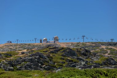 Serra da Estrela doğal parkının dağlarının tepesine bakın, kubbeli ve teleferik tramvaylı kule binaları, Star Mountain Range, kayalar ve bitki örtüsü ve dağ manzarası...