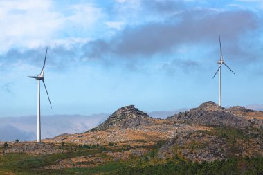 Dağların tepesindeki rüzgar türbinlerinin görüntüsü, arkaplan olarak bulutlu gökyüzü...