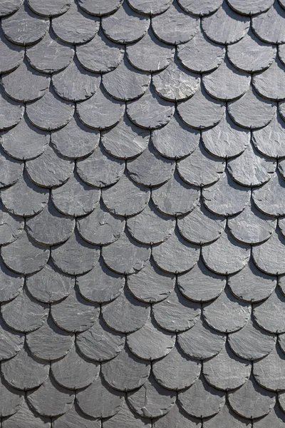 Detailed view of wall texture lined with slate-shaped fish scales from a building, typical and traditional schist stone material, used as external waterproof coating in the construction