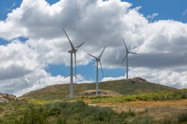 Dağların tepesindeki rüzgar türbinlerinin görüntüsü, arkaplan olarak bulutlu gökyüzü...