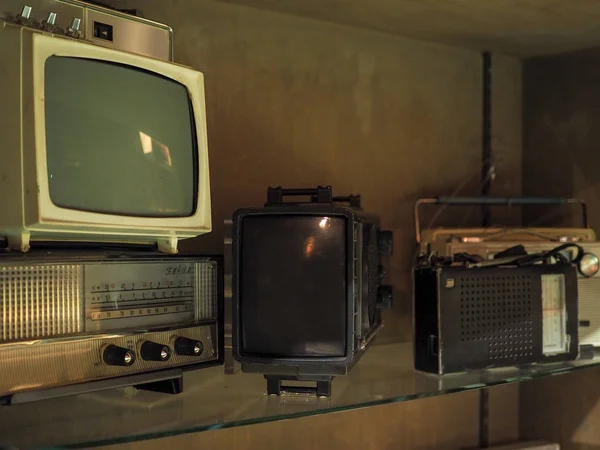 Old televisions and radios on a shelve.
