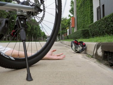 Yerde yatan bir bisiklet kaskının yakın çekimi ve yolda elini gösteren bir erkek cesedi. Seçili odak.