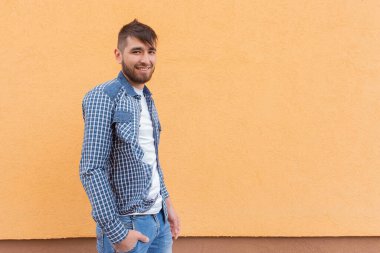 Turuncu duvara yaslanmış güzel ve mutlu adam.