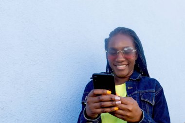 Mavi arka planda telefonu olan mutlu Afrikalı Amerikalı.