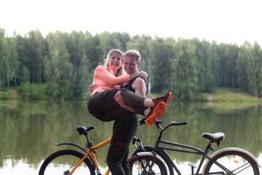 Birbirine aşık bir çift nehir kenarında bisiklete biniyor.