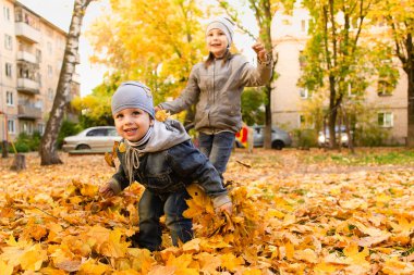 Mutlu çocuk ve kız sonbahar yapraklarında oynuyorlar.