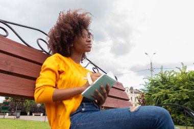 Parktaki güzel ve mutlu Afrikalı Amerikalı kadın, bir deftere notlar alır.