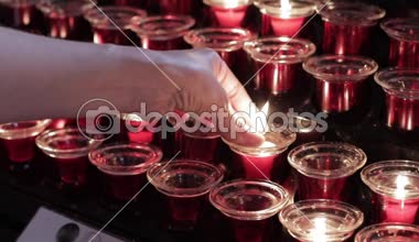 Genç bir kadın eli, Hıristiyan kilisesindeki kırmızı cam bir mum tutacağına yanan bir mum koyar.