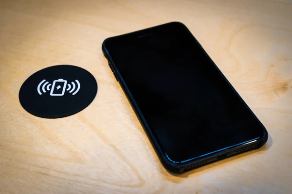 Smartphone charging on a table with a wireless charging pad. Wireless charging in common spaces like airports, cafes and stations concept