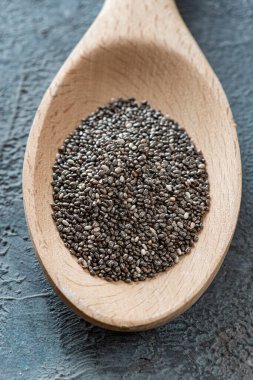 Gri bir yapının üzerindeki hafif bir tahta kaşıkta, yukarıdan bakıldığında, çok yakından görülen bir chia tohumu yığını..