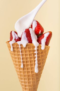Waffle külahında, damlayan beyaz yoğurt kremiyle kaplı çilekler.