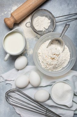 Mutfakta, gri desenli arka planda, bazı çatal bıçaklar, un, süt ve yumurta ve çeşitli malzemeler ev yapımı yemek tarifleri için hazır.